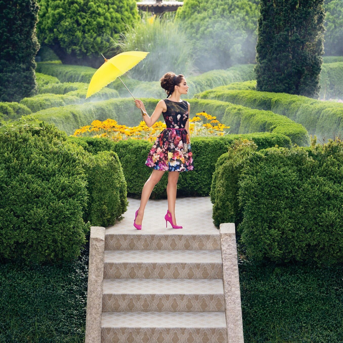 A woman standing on top of a stairwell in front of a garden fountain.